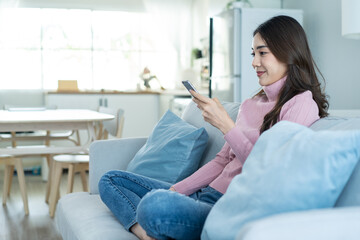 Wall Mural - Asian beautiful woman sit on sofa and chat on mobile phone in house. 