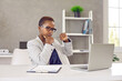 © Studio Romantic - Short haired black woman in glasses sitting at working table in office, looking at laptop computer screen with pensive face expression, reading article, doing fact checking, thinking, considering idea