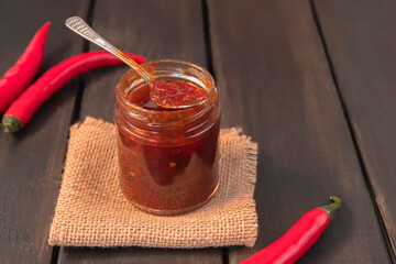 Hot pepper jam in a glass jar on dark wooden table, selective focus, copy space