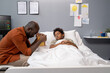 © pressmaster - African father holding the book and praying for health of his son while he lying in bed and sleeping at hospital ward