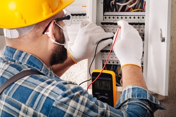 Wall Mural - Electrician at work on an electrical panel protected in safety goggles and gloves; Coronavirus. Construction industry. Covid 19 Prevention.