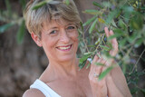 Fototapeta Na drzwi - Frau lächelt mit blauen Augen zwischen den Zweigen eines Olivenbaumes mit Oliven