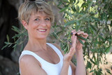 Fototapeta Na drzwi - Frau lächelt mit blauen Augen zwischen den Zweigen eines Olivenbaumes mit Oliven