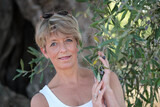 Fototapeta Na drzwi - Frau mit blauen Augen zwischen den Zweigen eines Olivenbaumes mit Oliven