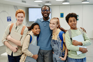 Portrait of male African-American teacher posing with diverse group of children in class and smiling at camera