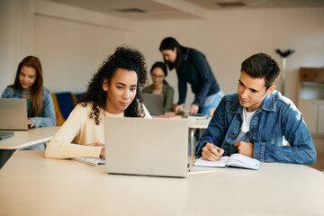 Wall Mural - High school classmates take notes while e-learning on laptop in classroom.