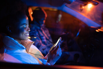 Gadget addicted couple sit in car on parking in silence using smartphones and surfing social media. African american man and woman busy with mobile phones while spending time together. Selective focus