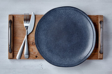 Wall Mural - Empty ceramic dark plate with cutlery on a brown wooden tray