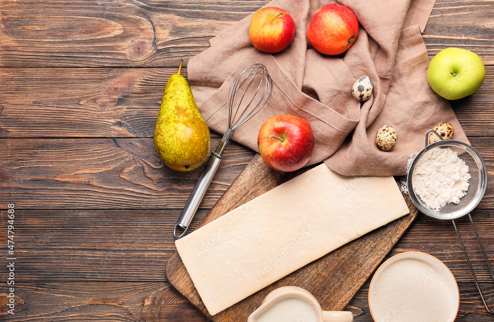 Board with fresh dough and ingredients for apple strudel on wooden background