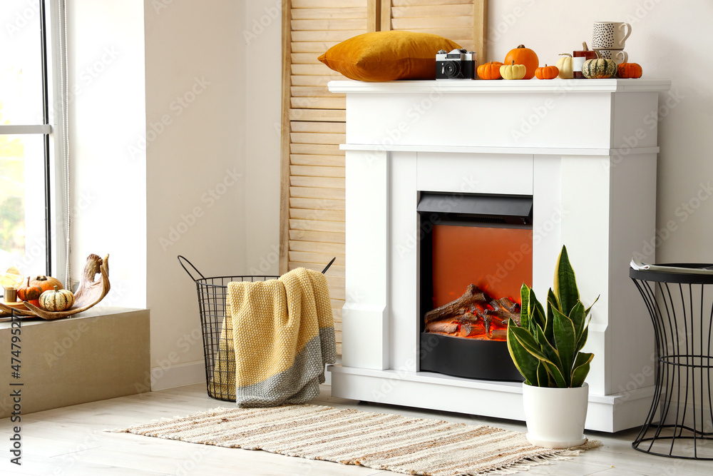Interior of light room with modern fireplace, pumpkins and basket