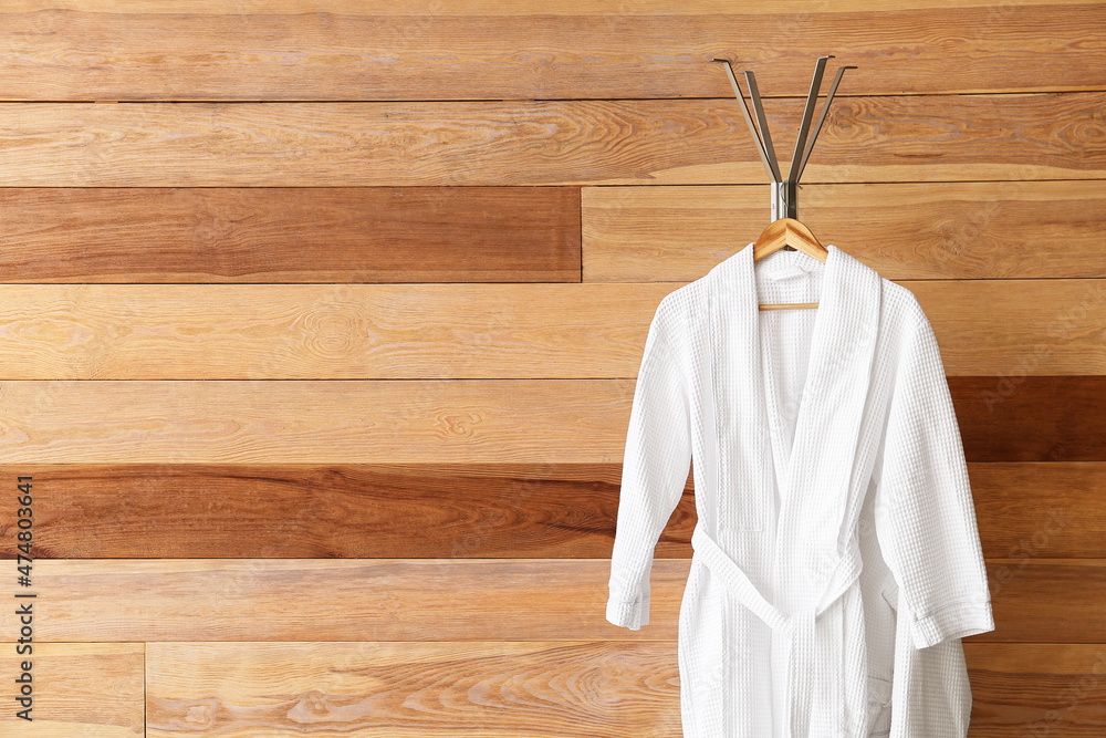 Rack with white bathrobes near wooden wall