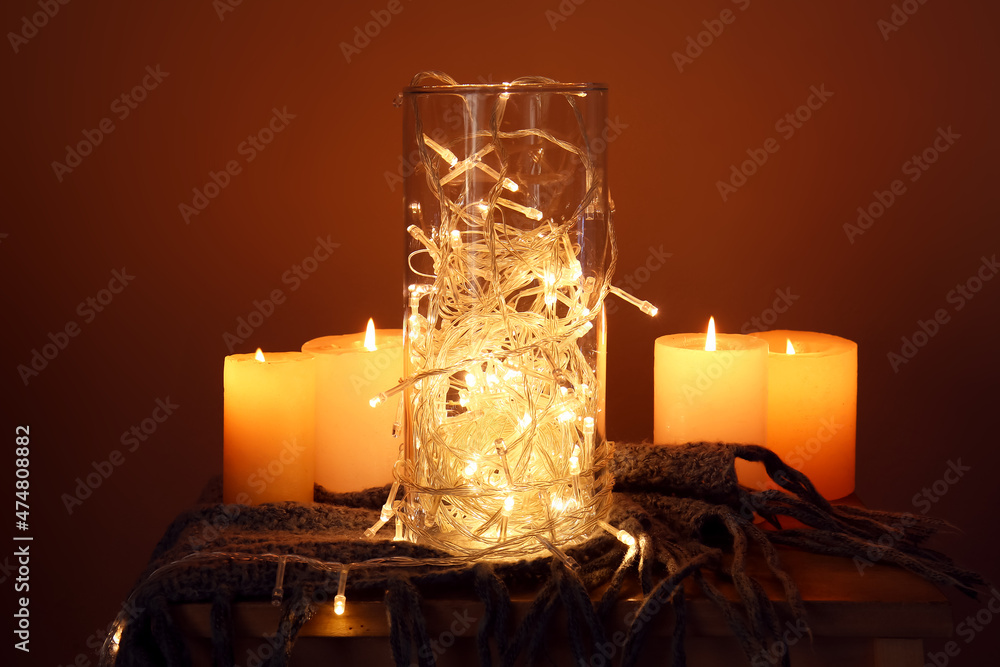 Glass with beautiful Christmas lights on table near light wall