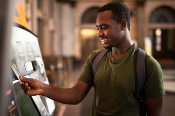 Wall Mural - Smiling African man using ATM machine. Happy young  man withdrawing money from credit card at ATM