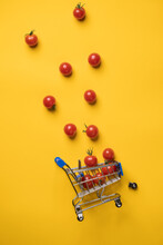 Overturned Decorative Grocery Cart And Cherry Tomatoes That Fell Out Of It, A Fallen Wheel Next To It, Against A Yellow Background. Top View. 