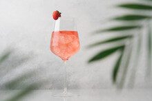 Glass Of Pink Cold Cocktail With Ice Surrounded By Palm Leaves. Summer Refreshing Drink On White Background, Side View, Close-up View