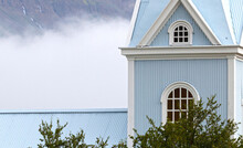 Wooden Blue Church In The Mist, Dwarfed By The Mountain Behind