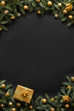 Christmas Vertical Frame With Gold Gift, Baubles, Evergreen Branches On Black Background With Copy Space. Xmas Greeting Card. Happy New Year. View From Above, Flat Lay.