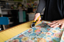 Closeup Of A Woman Cutting Fabric At A Table With Fabric Cutter For A Sewing Project 
