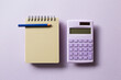 Beige notepad and calculator isolated on purple background. top view, copy space