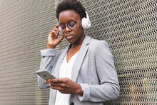 Black Businesswoman Listening To Music On Smartphone In Headphones