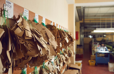 Close up shot of different paper and cardboard sewing patterns for leather boots and sneakers hanging on peg rack in workshop at shoe making factory. Concept of footwear manufacturing industry