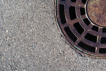 Sewer Round Hatch With A Grate On An Asphalt Road.