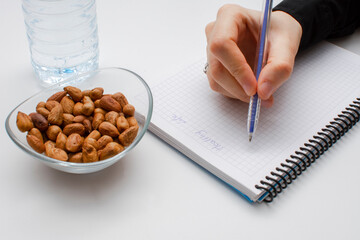 Student hand holding pen and writing notes in the notebook and glass bowl of hazelnuts and water bottle isolated