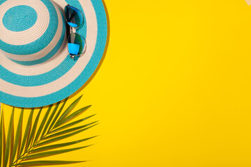 Wall Mural - Top view on beach accessories on yellow background - sunglasses, striped blue hat and palm leaf. Concept of beach holiday, sea tour, warm sunny summer. Advertising space