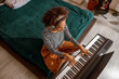 © Yaroslav Astakhov - Multiracial young woman sitting on bed and playing melody on synth musical instrument