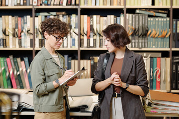 Sticker - Young contemporary shop assistant making notes about preferences of client while consulting her and helping to make right choice