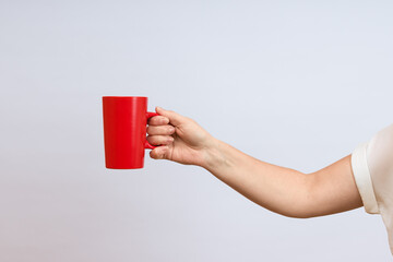 Wall Mural - female hand holding ceramic red cup on white background