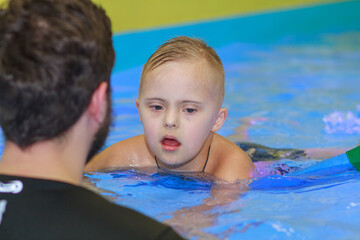 A boy with Down syndrome learns to swim in the pool, rehabilitation of disabled children, genetic anomaly, psychiatric congenital disease.
