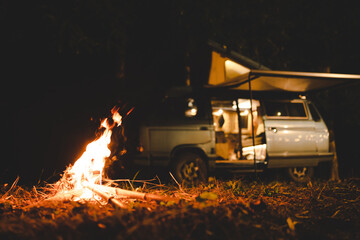 camping concept with camper van and fire at night under the tree in the forest mountain field