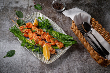 Wall Mural - Grilled king prawns with lemon and herbs on a plate against a gray stone table, fish kebab