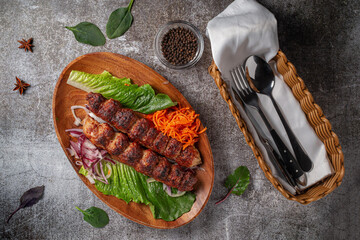 Wall Mural - Meat kebab and barbecue with onions, Korean carrots and green salad in a plate against the background of a gray stone table 
