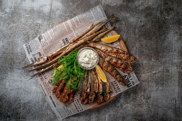 Sticker - An fish appetizer in a restaurant, fried sprat on a wooden plate with lemon and cream sauce against a gray stone table 