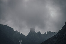 Dark Atmospheric Mountain Landscape With Black Pointy Rocky Peak In Gray Cloudy Sky. Lead Gray Low Clouds Among Black Mountains. Dark Rocky Pinnacle In Low Clouds In Rainy Weather. Gloomy Minimalism.