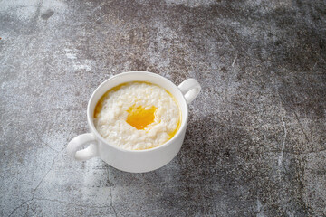 Wall Mural - Rice porridge with butter in a white cup against a gray stone table. A healthy breakfast in a restaurant .