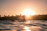 Fototapeta Sawanna - Portrait of blond surfer girl on white surf board in blue ocean pictured from the water at golden sunrise time in Encuentro beach