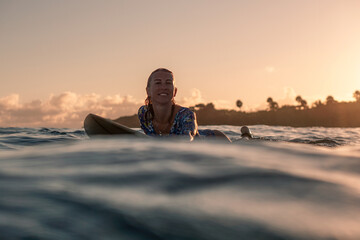 Wall Mural - Portrait of blond surfer girl on white surf board in blue ocean pictured from the water at golden sunrise time in Encuentro beach