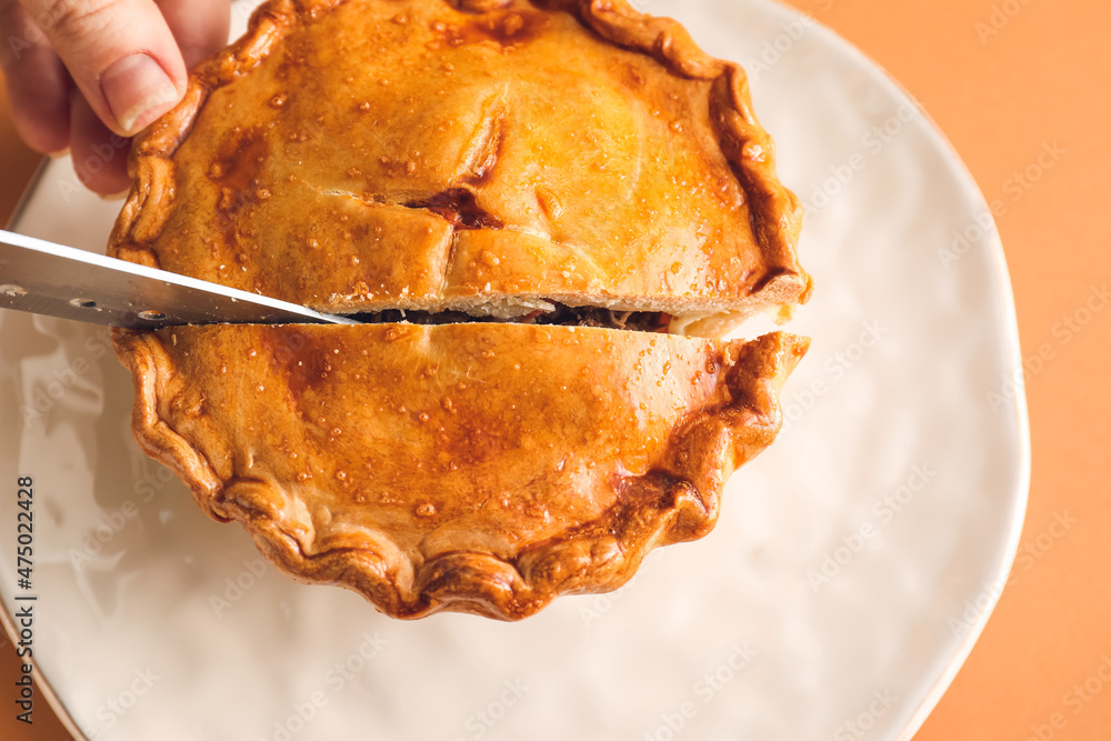 Woman cutting tasty beef pot pie on plate, closeup