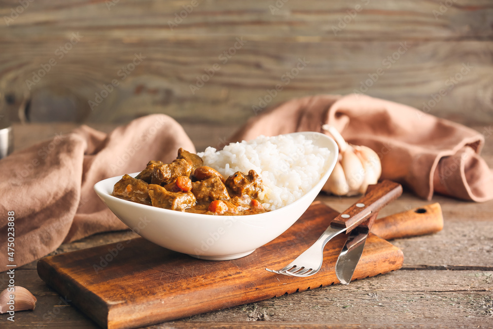 Plate with tasty beef curry and rice on wooden background