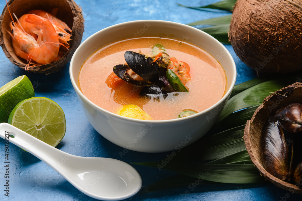 Bowl of spicy Thai soup on color background