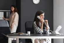 Young Woman Gossiping While Talking By Phone In Office