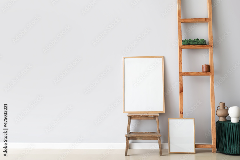 Blank poster on step ladder with decor near light wall