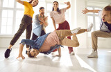 Talented youth. Young male dancer demonstrates his talent dancing breakdance in studio among other dancers. Group of positive people perform hip hop movements. Sport, dancing and urban culture concept