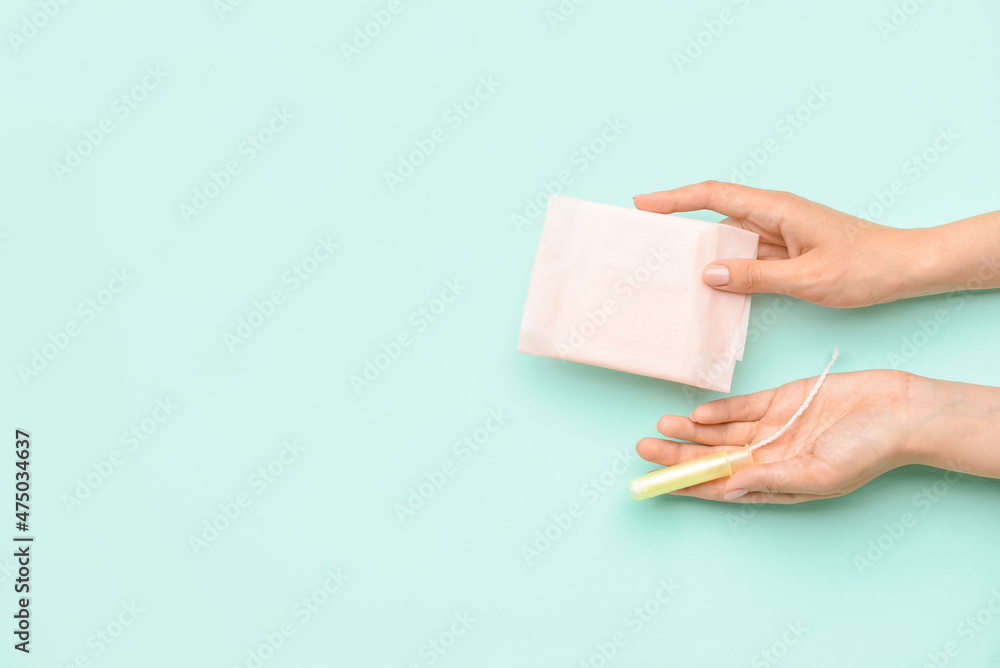 Female hands with menstrual pad and tampon on color background