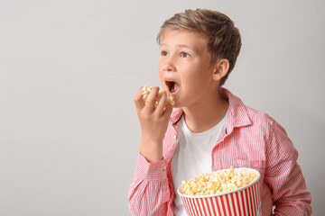 Poster - Little boy eating tasty popcorn on light background