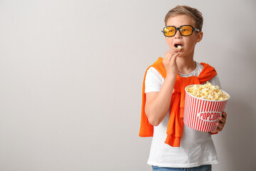 Sticker - Little boy in eyeglasses eating tasty popcorn on light background