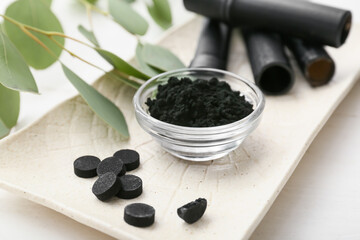 Bowl with activated charcoal tooth powder and pills on white wooden background